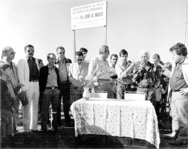 Água em Simonsen - Dotar o distrito de Simonsen de água tratada nas torneiras foi uma meta cumprida no governo de João Antonio Nucci em 1982. A foto registra o momento da assinatura do contrato para o poço profundo. Aparecem na foto, a partir da esquerda os vereadores José Nunes Pereira e Joaquim Lúcio da Silva,Nasser Gorayb, o superintendente da Saev Jesus Silva Melo, o vice-prefeito Onofre de Paula, atrás dele Júnior Ferrari,o prefeito João Antonio Nucci, atrás dele o Toninho da Artésia, radialista Édson Palmiéri, o chefe de gabinete Edward C. Costa (discursando), atrás deleToninho Guerche e o radialista João Carlos Ferreira.