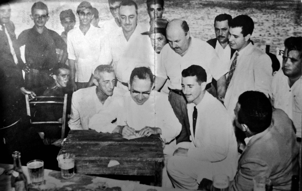 Esta foto é histórica. O ano é 1956 - na semana do Natal. E com esta assinatura do deputado estadual Dr. Anísio José Moreira nasceu a Associação Atlética Votuporanguense- uma das glórias do futebol do interior. Existiam na cidade dois times rivais. O VEC - Votuporanga Esporte Clube tinha como presidente o Sr. José Silva Melo (Zéquinha Alfaiate), e o América Futebol Clube, na época sob a presidência do Rachidinho (funcionário da Prefeitura Municipal). Os homens que aparecem nesta foto foram os articuladores da fusão, os responsáveis direto pelo surgimento da AA Votuporanguense. Confira a partir da esquerda quem são esses pioneiros do esporte. Em pé: Nélson Maraldi, Ozório Casado, Arquimedes Neves (o Nei), ? , Moacir Másquio (Nininho), Vicente Castrequini, Lula, Zézinho Marão, dr. Martiniano Salgado, ? , Carlos Márcio de Castro Junqueira, e Deolindo Trindade (Frinfa). Agachados na mesma ordem: o primeiro não identificado, Alfredo Rodrigues Simões (Cavaco), ao centro o deputado estadual Dr. Anísidio José Moreira, Plínio Marin, e de costas Emílio Liévana Torres (o Torrinha). A foto pertence ao ex-vereador Ozório Casado e a identificação das personalidades foram feitas pelo nosso colaborador Dagoberto José Mira Alves (Dago).