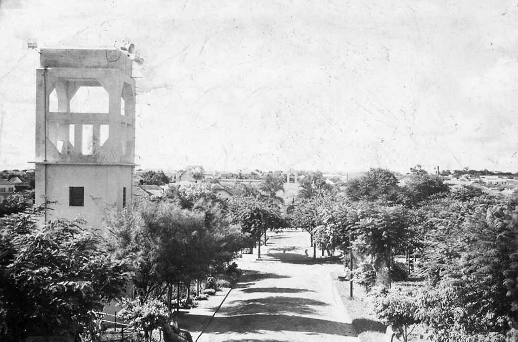 O famoso Foto Paramont foi o autor desse registro fotográfico na década de 1950. É uma visão do Jardim da Matriz, a partir da rua Alagoas. Na época, existia uma torre de Serviço de Alto-Falante (veja à direita), onde anunciavam notícias da cidade, pessoas, eventos sociais e hora certa. No meio do jardim, havia o famoso “coreto” onde certa feita, o aviador Vicente Lupo fez um pouso de emergência por causa de falhas mecânicas no motor do avião. Veja ao fundo, depois do coreto, a 1ª Igreja de Votuporanga, que foi derrubada após a construção da atual Matriz (Nossa Senhora Aparecida). Esta imagem tem mais de 64 anos de existência e pertence ao arquivo pessoal do antigo morador de Votuporanga, Luiz Carlos Murasse, que também é o autor desta legenda com todas as informações. Agradecemos a colaboração.