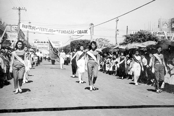 Desfile do dia 8 de agosto dos anos 50. Da esquerda para a direita: Marlene Mantovani e Javicene. Na fila do meio: Ana Maria Buck, Lurdinha Rocha e Cleide Perese. Na fila da direita: Adnéia, Marisa Mantovani e Maria José. Na rua Amazonas, ainda de terra, veja à direita a Igreja Matriz em construção. A foto e do arquivo pessoal de Rames Cury e Maria Antonia.