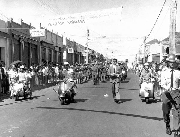 O desfile cívico-militar dos anos 60. A novidade era a chegada da Vespa (um modelo diferenciado da lambreta) que abria o desfile do Batalhão Militar. Veja detalhes do comércio da rua Amazonas. Na esquerda a identificação da Livraria Belloni e o Foto Kodak, do Takeo Sato. A faixa em cima é da empresa Irmãos Marão.