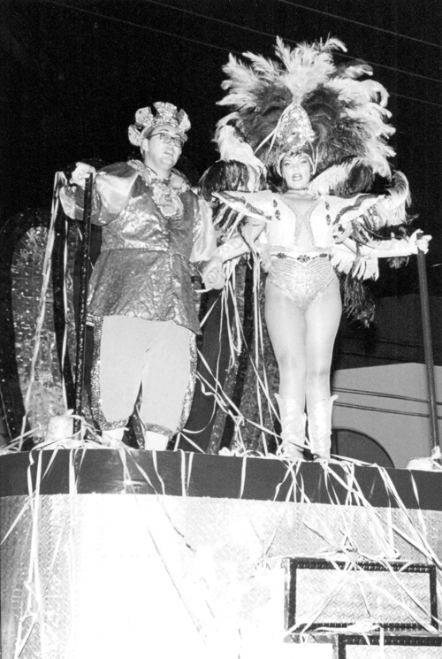 O galã e a debutante -  O tema é Carnaval. Trata-se de um desfile de rua da década de 90, mais precisamente em 1998. No carro alegórico oficial, a sua majestade o Rei Momo Juliano Bombom e a Rainha Adriana.