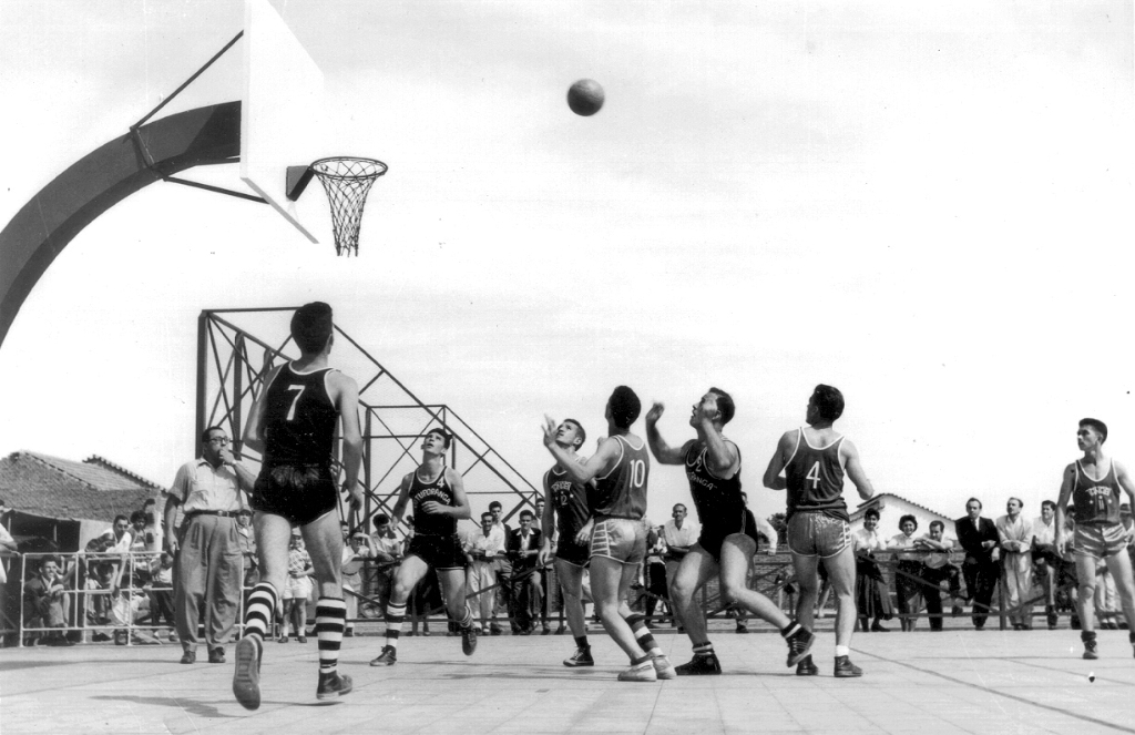 A foto é de 1957 e mostra um lance do jogo de basquete que marcou a inauguração da quadra do Votuporanga Clube. Aparece o árbitro do jogo, o comerciante João Kecheuguerian (em memória), mais conhecido por João da “Armênia” - loja de calçados então localizada na rua Amazonas, onde hoje é a Casas Bahia. Em destaque os jogadores: Walter Costa, Antonio Moretti (em memória), Laércio Ceneviva (em memória) e outros jogadores de Tanabi (time adversário). A foto é do arquivo particular de Walter Costa.