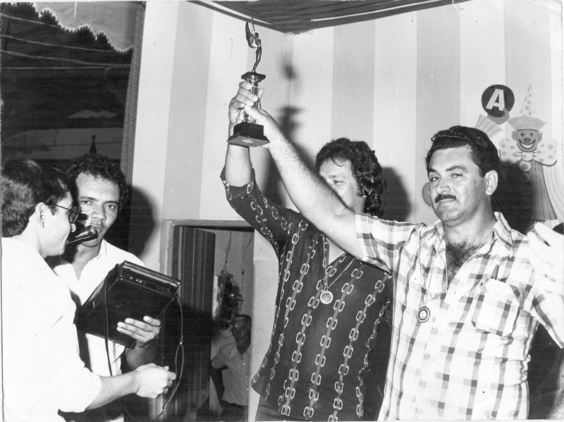 Truco no Assary - Os campeões levantam o troféu. Era a final do Torneio de Truco, no Assary Clube de Campo, no ano de 1975. A foto registra a consagração dos vencedores João Luvian Matheus e Moacir Munhóz (a direita).Enquanto isso, o então presidente do clube, Darcy Pereira de Moura, concedia uma entrevista ao popular repórter da Rádio Clube, Beny Andrade. Este hoje trabalha numa grande emissora de rádio na cidade de Porto Velho-RO. A foto pertence ao arquivo pessoal de João Luvian Mateus (João da Garagem).