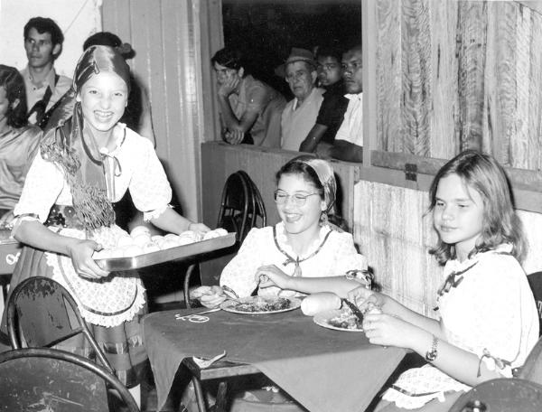 Nos anos 70 a Colônia Italiana arrasou com a sua juventude na Festa das Nações. O destaque nesta foto é para as meninas em traje típico (e mostrando serviço na arte de bem servir) o apreciado cardápio italiano. Aparecem na foto Séfora Comar, Laurinha Ayres e Celi Vendramini. A foto pertence ao arquivo pessoal da família Tannuri Ayres.\r\n