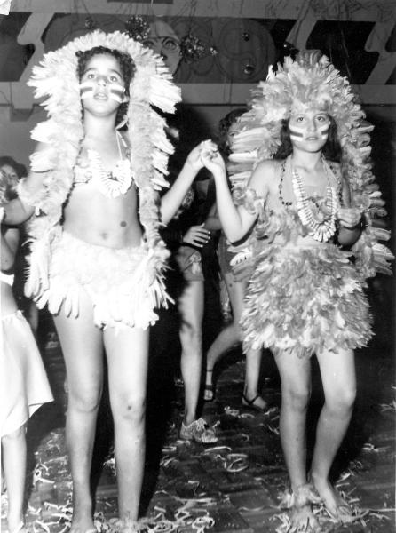 Salão do Votuporanga Clube decorado com motivos carnavalescos, no chão confetes e sepertina e em primeiro plano as meninas em traje indio. É um retrato das grandes vesperais carnavalescas de Votuporanga. A foto é do ano de 1974.As personagens da foto são Laurinha Ayres e Sonia Rosicler Trindade. A foto pertence ao album da  família Ayres.